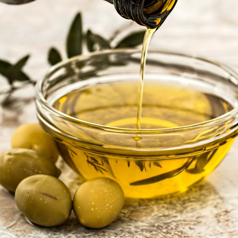 Olive oil being poured into a glass bowl with olives