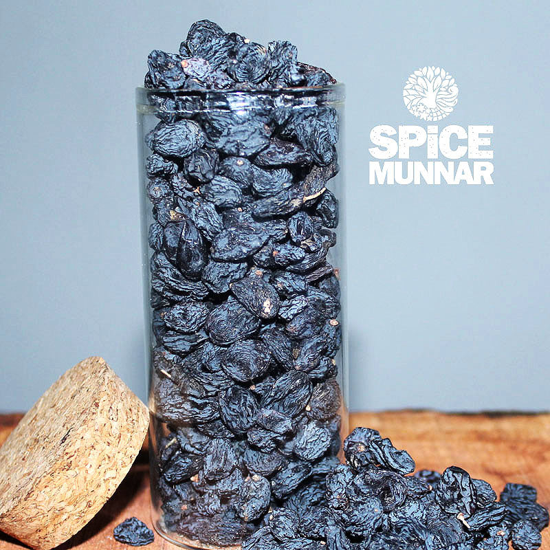 Glass jar filled with black raisins on a wooden surface with 'Spice Munnar' branding.