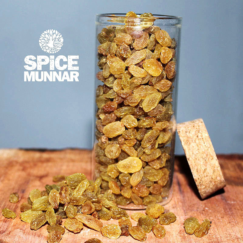 Glass jar filled with raisins on a wooden surface, with 'Spice Munnar' branding.