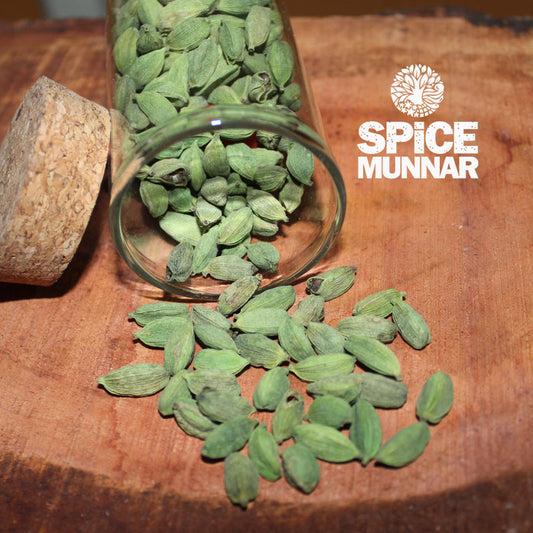 Green cardamom pods spilling out of a glass jar with 'Spice Munnar' branding.